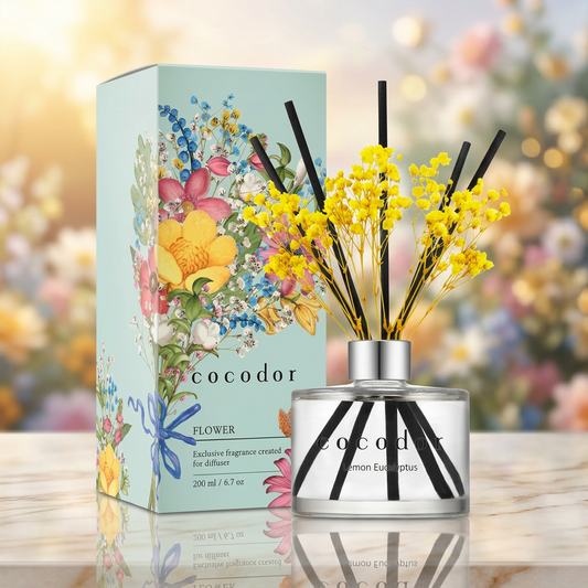 Αρωματικό χώρου Cocodor Flower Diffuser με κίτρινα λουλούδια και μαύρα sticks δίπλα σε γαλάζια συσκευασία με λουλουδάτα σχέδια, σε μαρμάρινη επιφάνεια - VassoHome