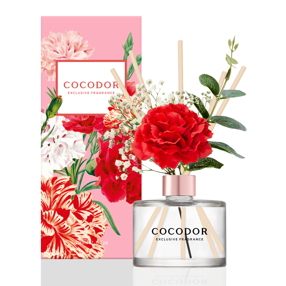 Αρωματικό χώρου Cocodor Carnation με κόκκινο γαρίφαλο, ξύλινα sticks και ροζ συσκευασία με σχέδια λουλουδιών σε λευκό φόντο - VassoHome 
