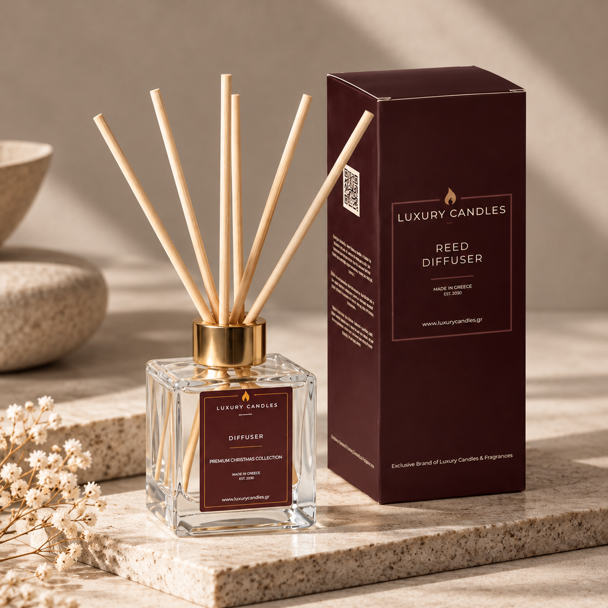 Αρωματικό χώρου Μελομακάρονο 100ml με ξύλινα sticks δίπλα στη μπορντό συσκευασία του, σε πέτρινη βάση με μικρά λευκά λουλούδια - VassoHome