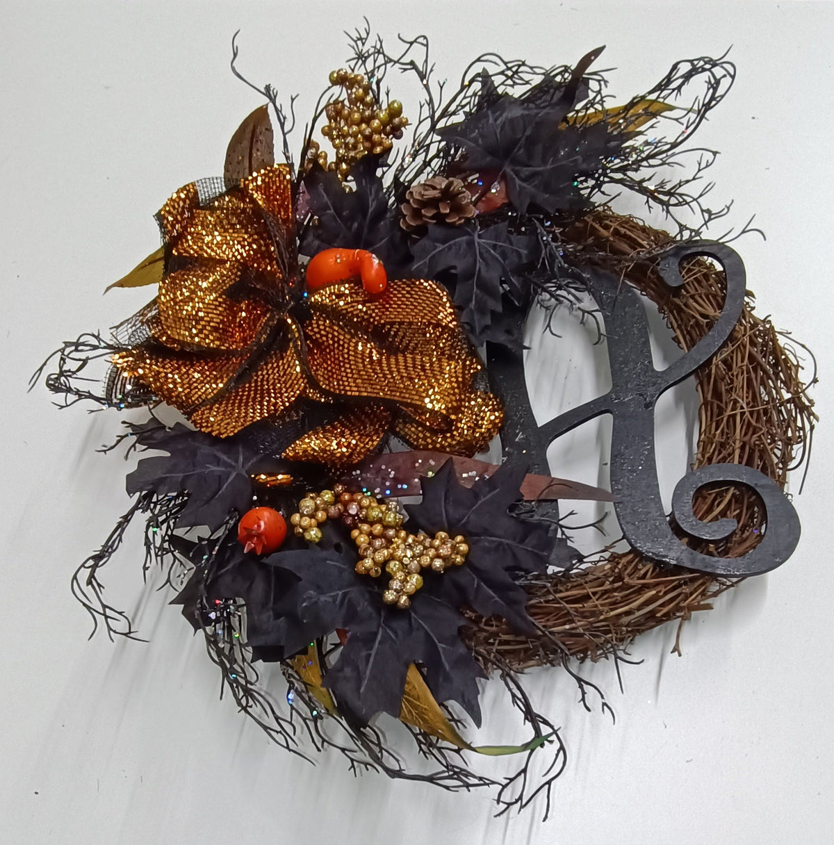 Halloween στεφάνι με μαύρα φύλλα, χρυσοπορτοκαλί φιόγκο, πινόκονες, χρυσά berries, πορτοκαλί κολοκυθάκια και μαύρο διακοσμητικό πλάγια γωνία σε λευκό φόντο - VassoHome